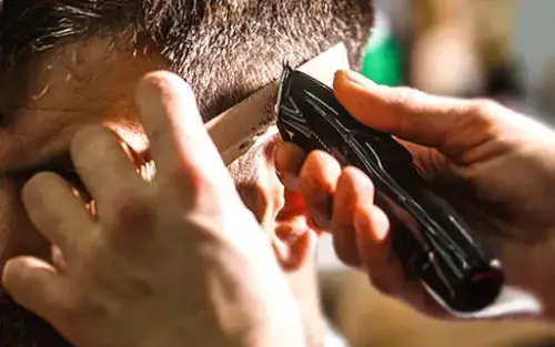 Barber completing detailed clipper-and-comb work around a client's temple