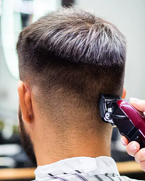Barber shaping a clean fade with clippers inside Dino's